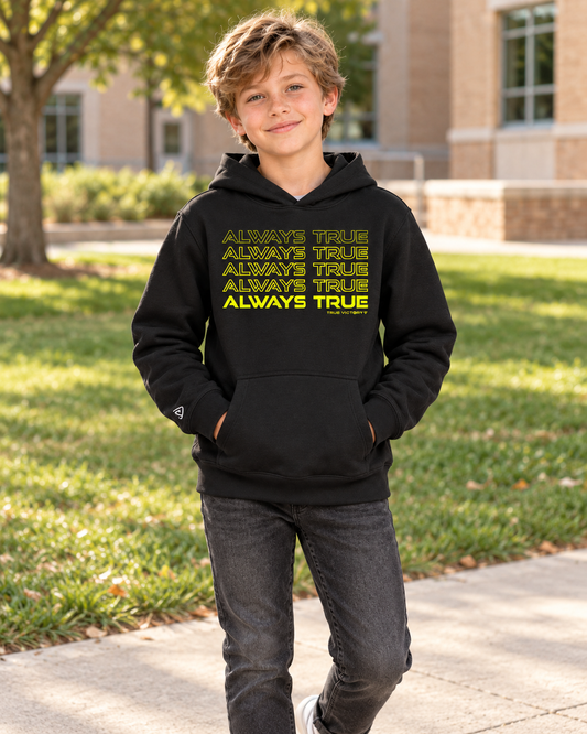 Boy wearing the black Youth Always True Stacked Hoodie with neon yellow lettering beside a school lawn