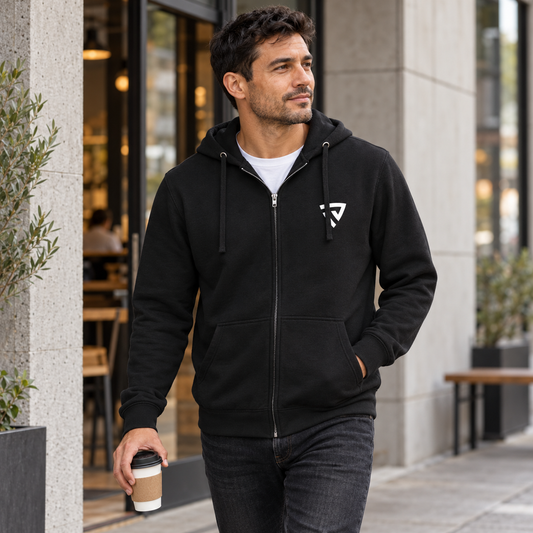 Man wearing the black Legacy Full Zip Hoodie outside a concrete city cafe.