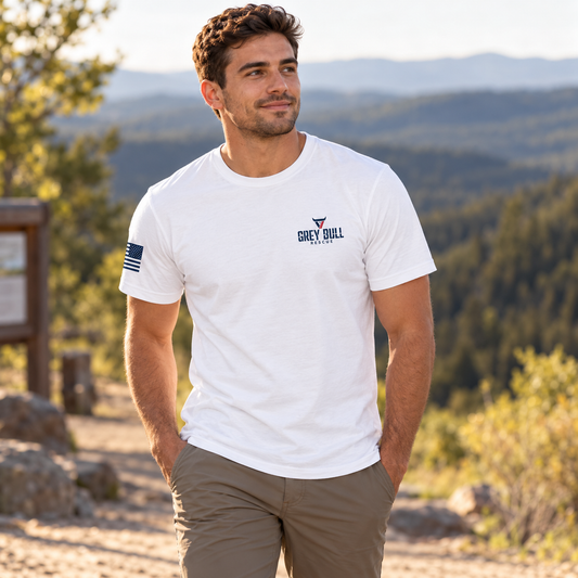 Grey Bull Rescue No Spectators White Tee worn by an adult man in an open trailhead with distant wooded hills in warm afternoon light; front view.