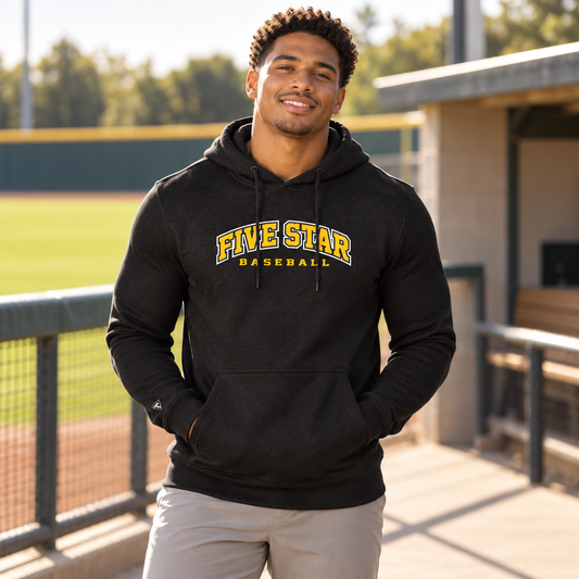 Man wearing the Five Star Baseball Black Hoodie beside a baseball field.