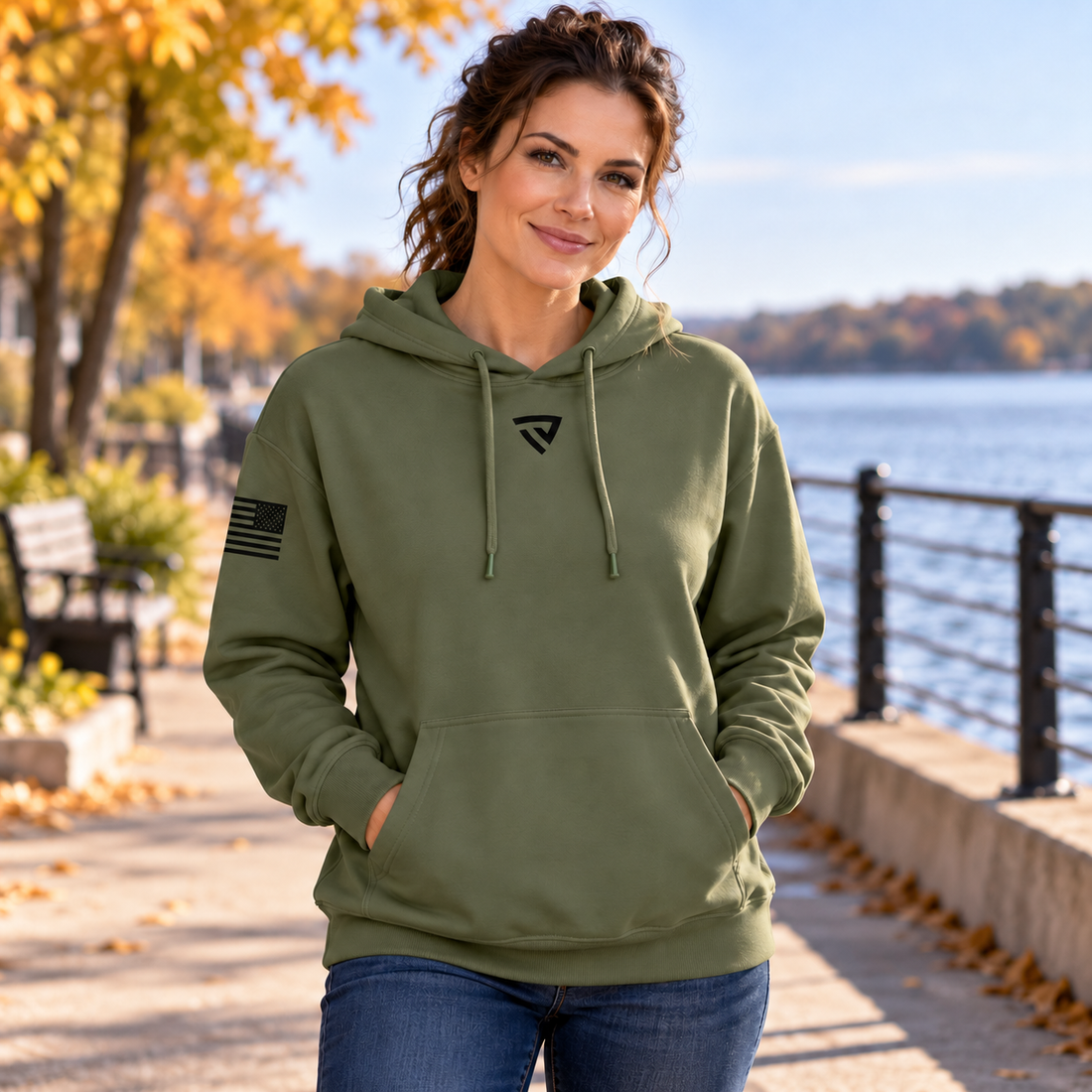 Woman wearing the military green Freedom Is Not Free hoodie beside a lake in autumn.
