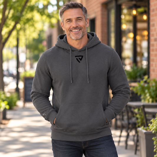 Men's Legacy Hoodie worn by an adult man in a tree-lined town walkway beside a softly blurred brick building and outdoor cafe; front view.