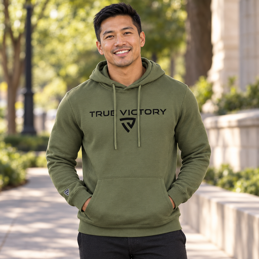 Men's Victorious Hoodie worn by an adult man in a quiet city park path with trees and minimal warm stone architecture; front view.
