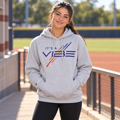 Woman wearing the gray It's a Vibe Softball Hoodie beside a softball field.