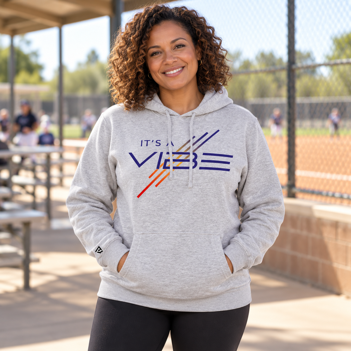 Woman wearing the gray It's a Vibe Softball Hoodie at a softball park.