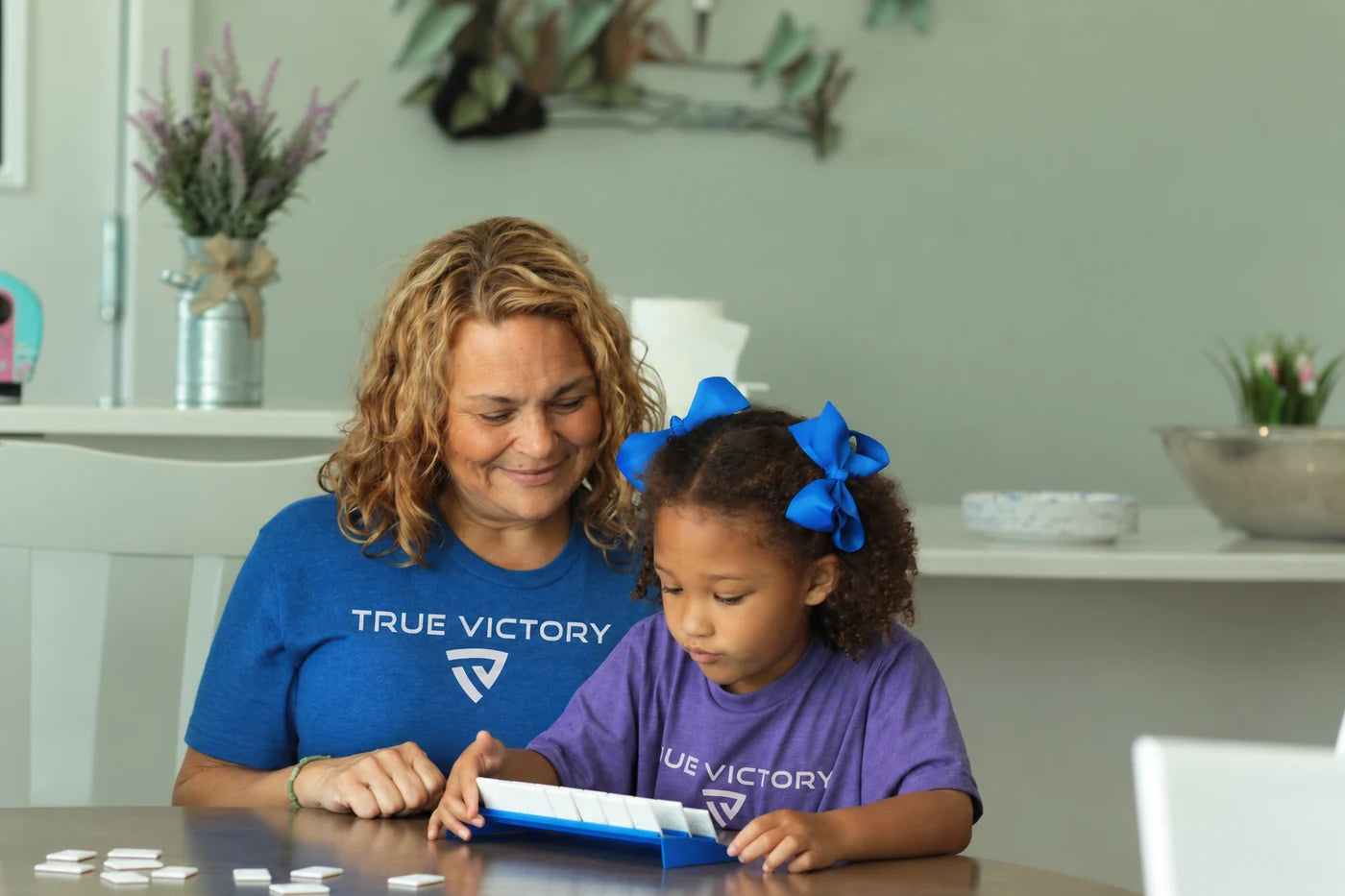 A woman and child sharing a table game in blue and purple True Victory tees.