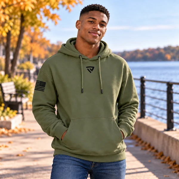 Young man wearing the military green True Victory hoodie beside a lake in autumn.