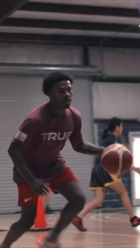 Basketball player wearing a maroon True Victory shirt while dribbling.